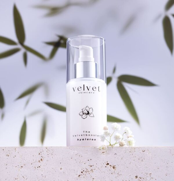 Velvetbooster Hyaluronserum auf Naturstein mit schwebenden Blättern – clean, minimalistisch, hautfreundlich