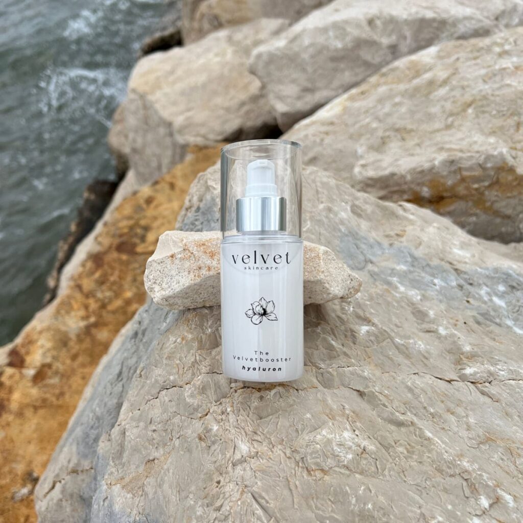 Velvetbooster Hyaluronserum von Velvet Skincare auf Felsen am Meer – cleanes Design, natürliche Hautpflege